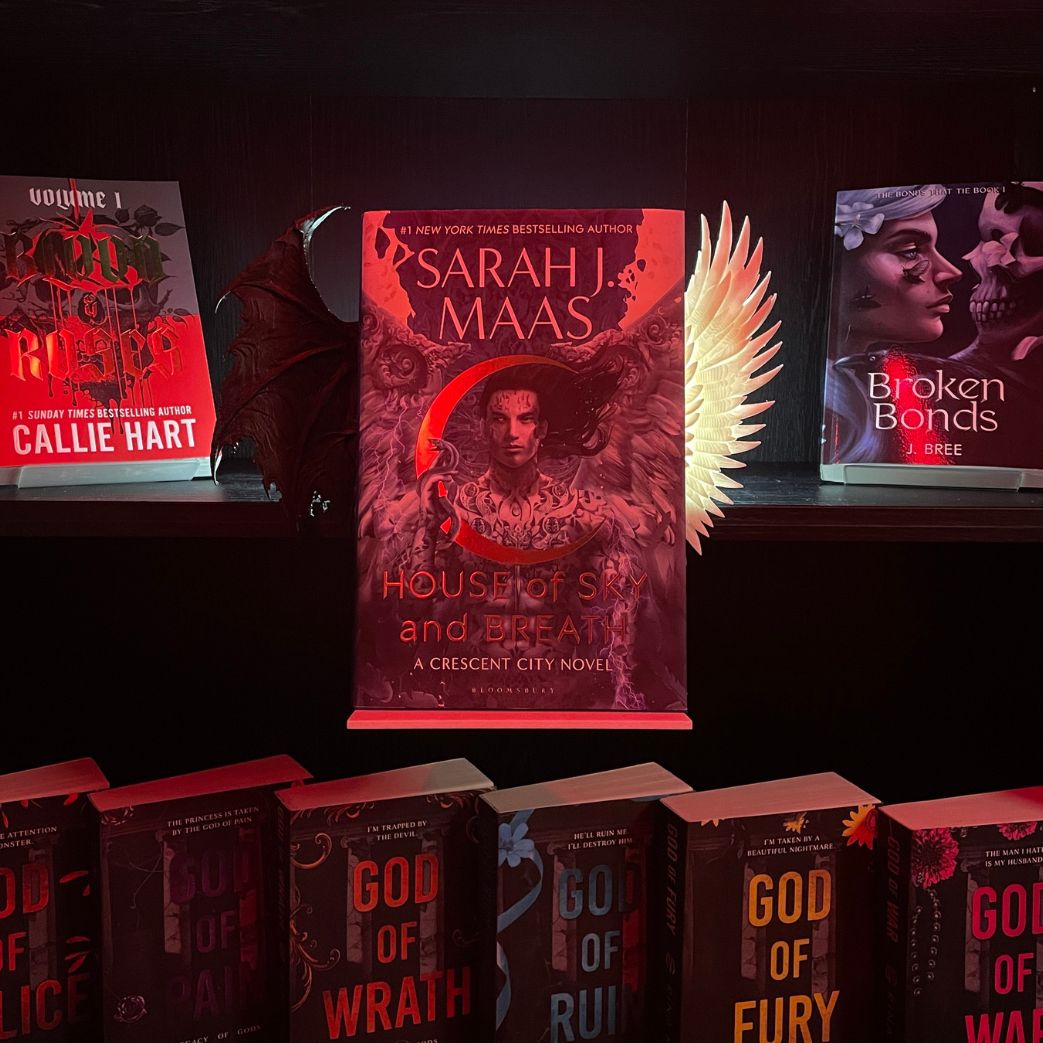 Hardcover book display featuring House of Sky and Breath by Sarah J. Maas mounted on a Curio Candy Floating Book Display Hanger with posable white Angel and black Gothic clip-on wings on a dark shelf.