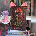Pink 3D printed Feline and Canine Ear Curio Clip-Ons peaking over the top edge of the shifter romance novel A Game of Cat and Witch by Ruby Rune on a white Floating Book Display Hanger.