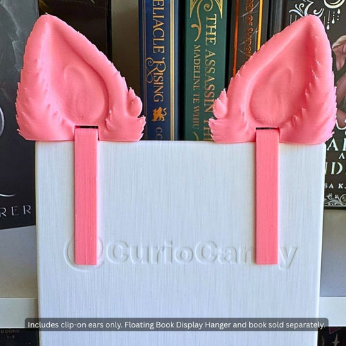 Detailed front view of pink 3D printed tufted Feline and Canine Ear Curio Clip-Ons attached to the rear plate of a Floating Book Display Hanger behind an 8-inch paperback.