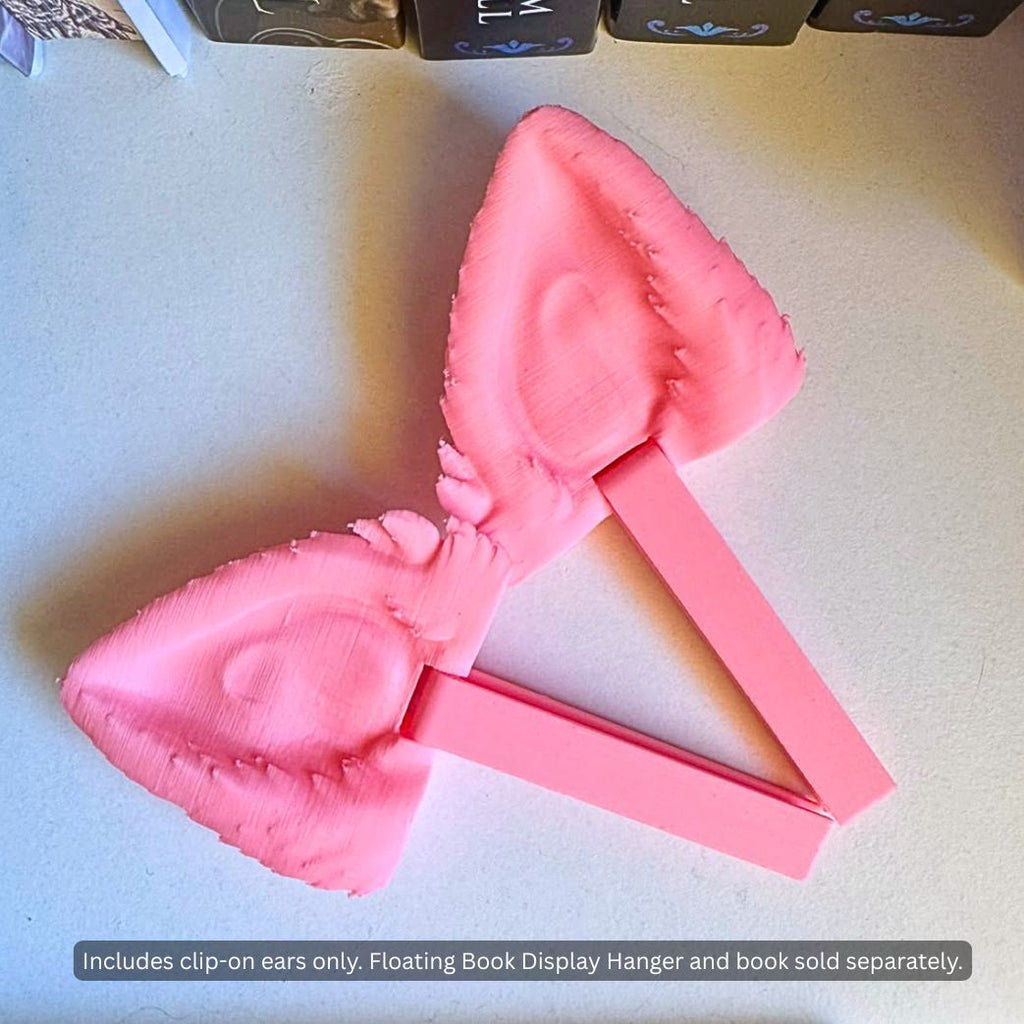 Pair of pink 3D printed Feline and Canine Ear Curio Clip-Ons lying flat on a white surface, showing inner ear sculpt detail, tufted edges, and attached back-mounting display arms.