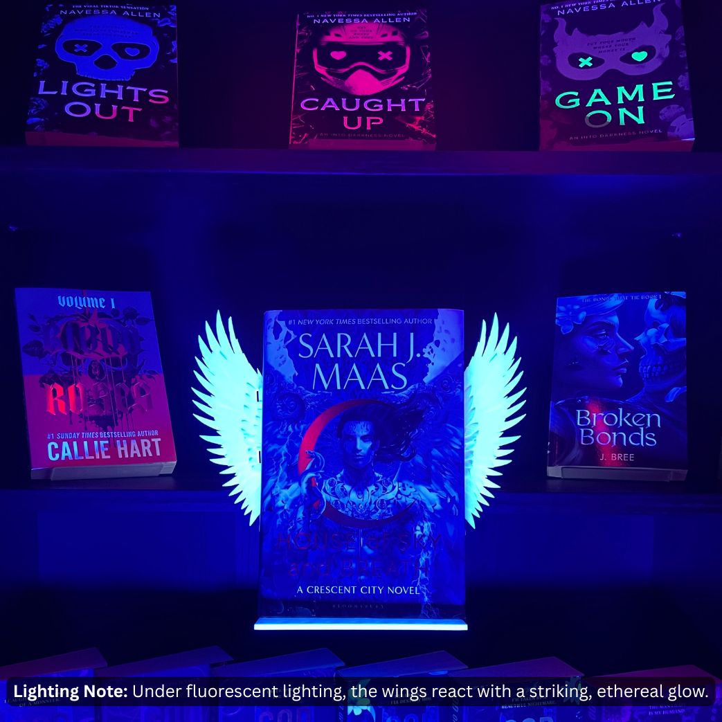 Curio Clip-On Angel Wings attached to a Curio Candy Floating Book Display Hanger, glowing under fluorescent front light on a dark romance bookshelf featuring Sarah J. Maas.