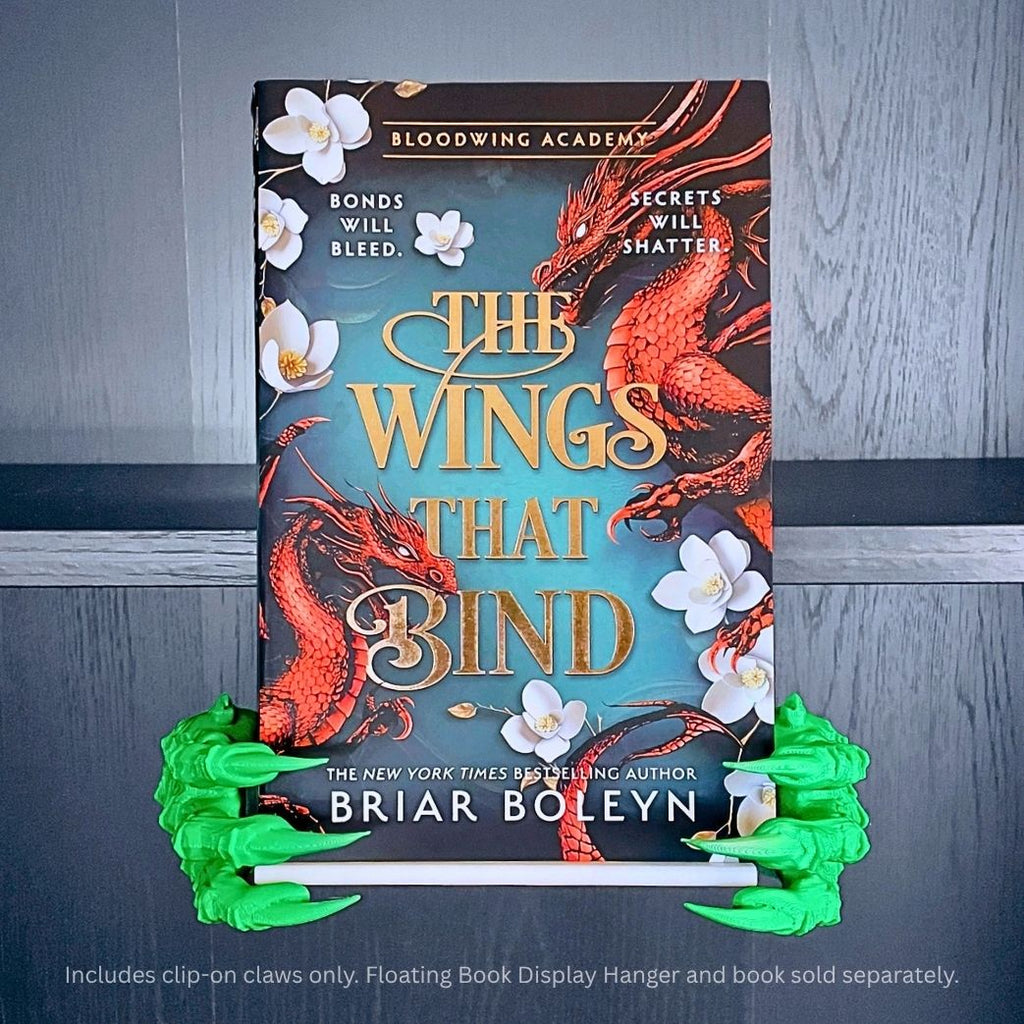 Green 3D printed Dragon Claws Curio Clip-Ons framing the fantasy book The Wings That Bind by Briar Boleyn, clipped onto a Curio Candy Floating Book Display Hanger.