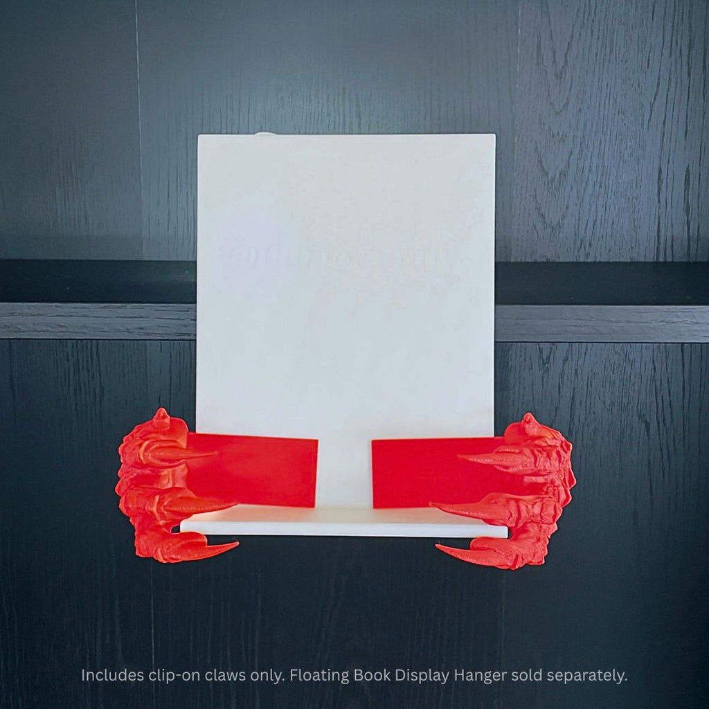 Red 3D printed Dragon Claws Curio Clip-Ons attached to a white Curio Candy Floating Book Display Hanger against a dark wood background with blue top backlighting.