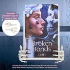 Bone-coloured 3D printed Skeleton Hand Curio Clip-Ons gripping the sides of the fantasy romance novel Broken Bonds by J. Bree on a white Floating Book Display Hanger, featuring an inset graphic showing the pair of clip-on hands.
