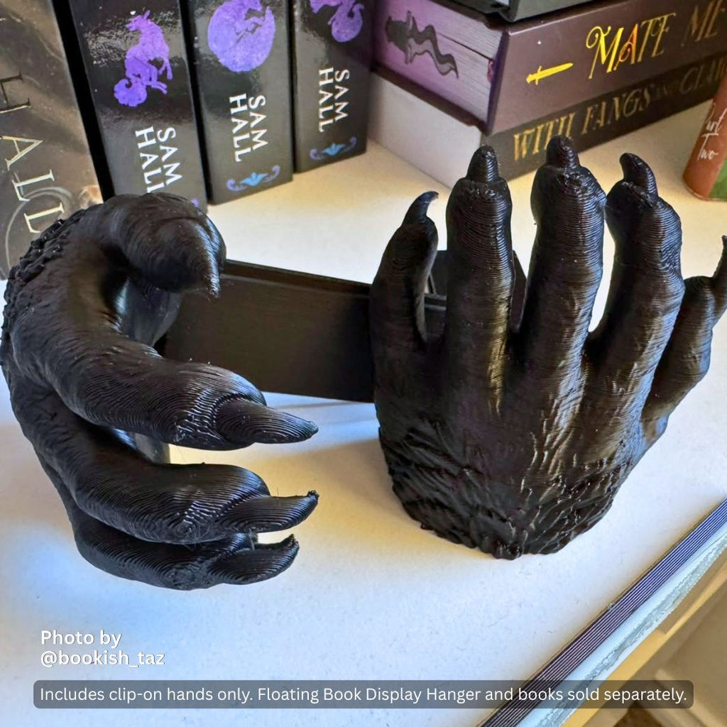 Black 3D printed Werewolf Hand Curio Clip-Ons gripping the sides of the fantasy novel The Court of the Dead by Rick Riordan and Mark Oshiro on a white Floating Book Display Hanger, featuring an inset graphic showing the pair of clip-on hands.