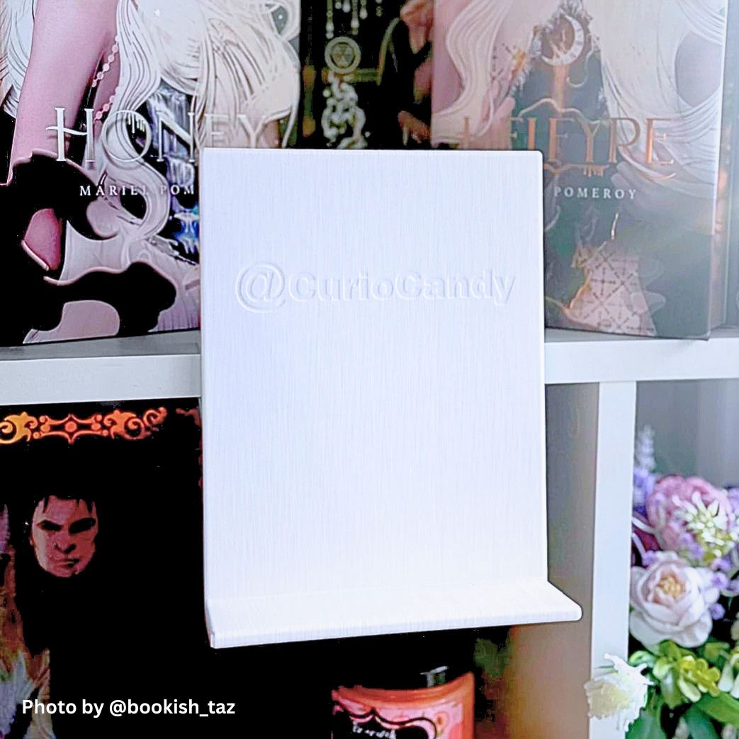 Curio Candy official branded white floating book display hanger showing embossed logo backplate on white bookshelf.